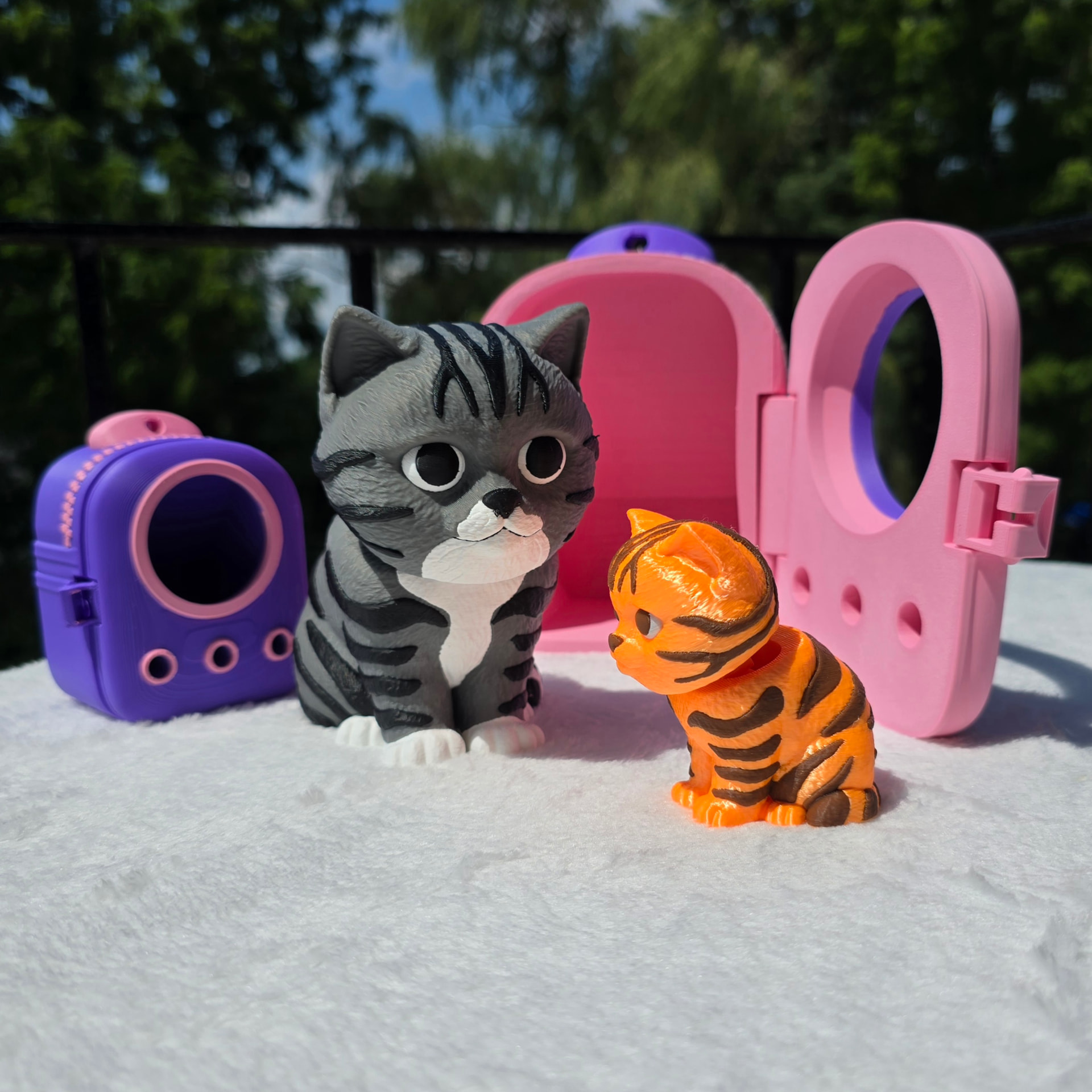 The 6 inch gray tabby and 3 inch orange tabby sitting side by side in the sun